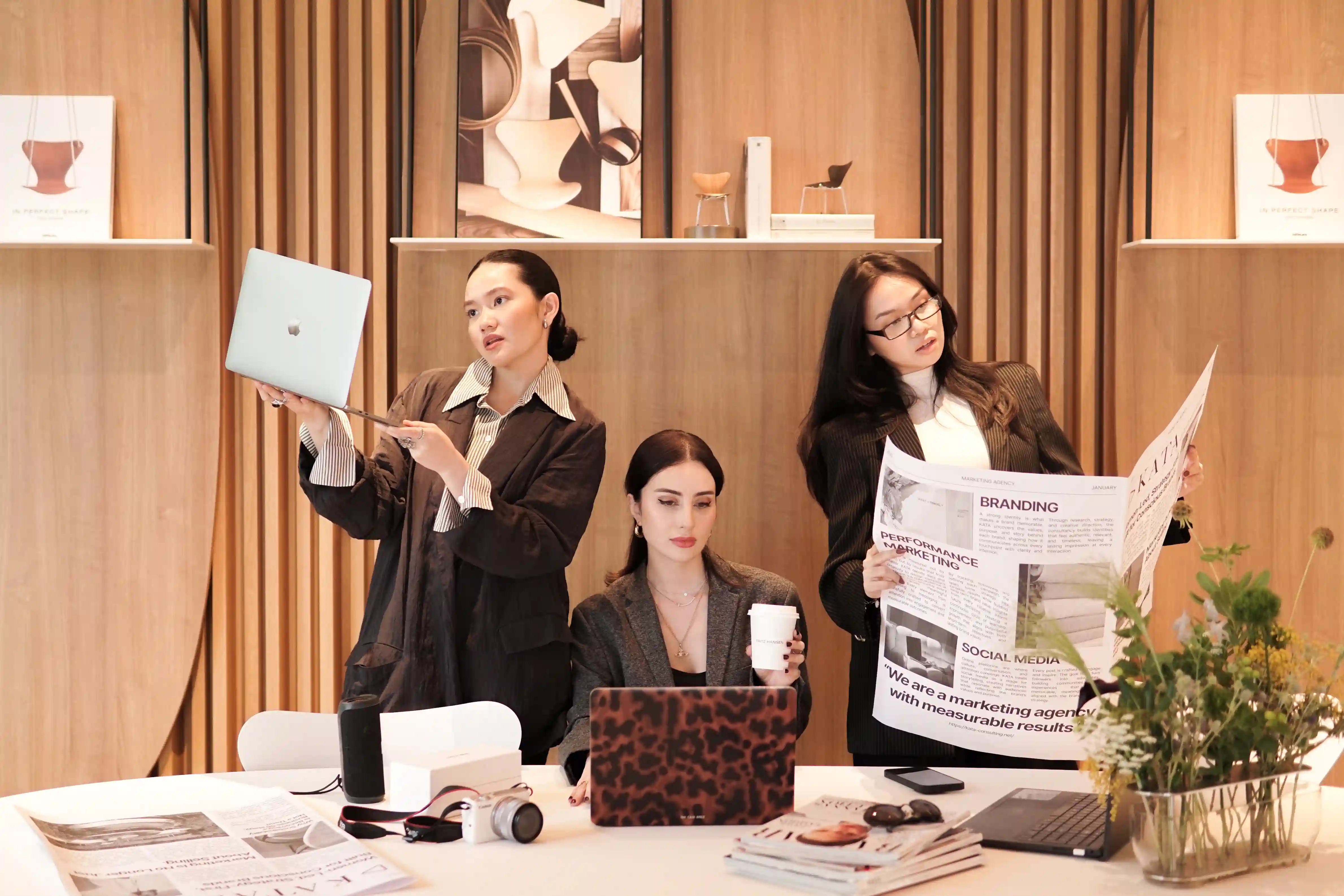 Three KATA team members gathered around two laptops on a dark wood table